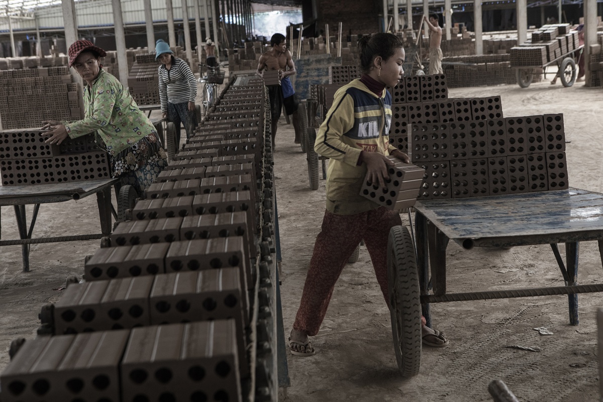 People at work on the conveyor belt of a brick cutting machine.
The expansion projects of large Cambodian cities require a large production of bricks. Factories use a labor force based on slavery. Debt bondage is a person's pledge of labour or services as security for the repayment for a debt or other obligation. This condition is passed on from generation to generation. In Cambodian brick factories, debt bondage is a normal condition and entire families live and work within the factories.