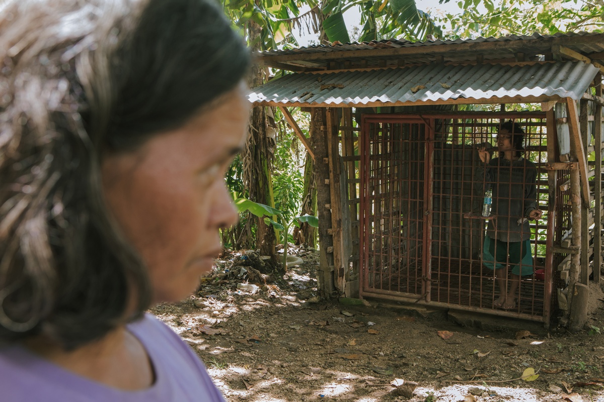 City: Bogo  Generic: Banban  State: Provincia di Cebu  Country: Filippine  - 24/09/2018 Victoria Ancao, in front of the cage where her 21-year-old nephew Jessie has been locked up since 2015. Jessie Bryan, 21, locked in a cage since 2015 by his mother and his aunt. One week's treatment at the psychiatric clinic in Cebu did not help to improve his condition. After returning home, his aunt Victoria Ancao did all she could to treat him and look after him. Unfortunately, having to work for the sustenance of the family, she was forced to close her nephew in a cage. 
